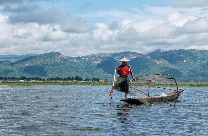 湖中心有漁夫單腳撐船同時撒網捕魚，划近湖邊的淺水沼澤有村民下水